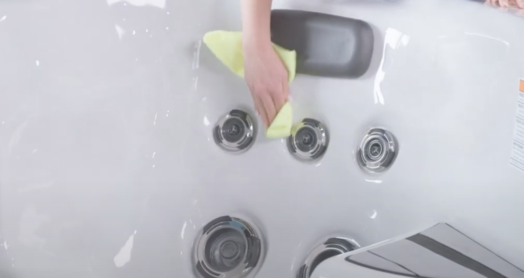 A woman cleaning a swim spa bathtub with a microfiber towel.
